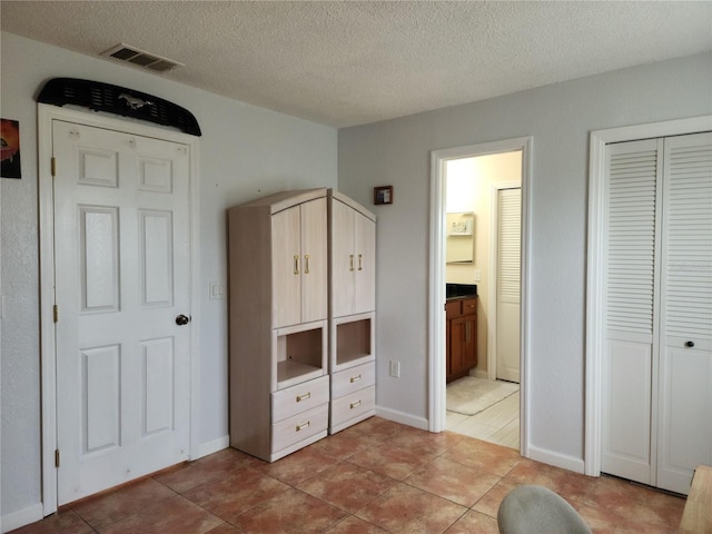 unfurnished bedroom featuring a textured ceiling, a closet, light tile patterned floors, and connected bathroom