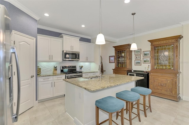 kitchen with white cabinetry, a center island with sink, appliances with stainless steel finishes, decorative light fixtures, and ornamental molding