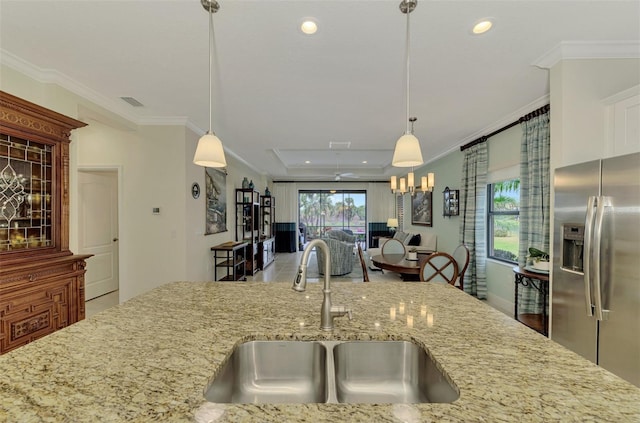 kitchen with light stone counters, sink, pendant lighting, and stainless steel fridge