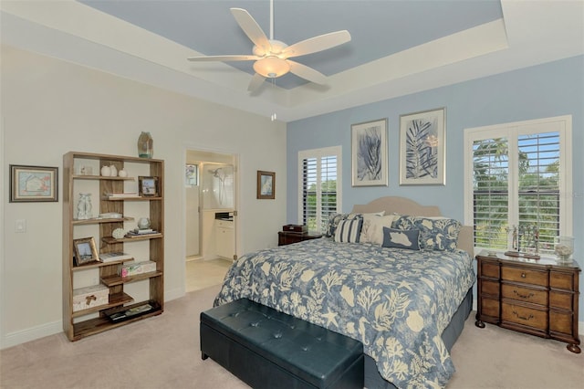 carpeted bedroom featuring ceiling fan, multiple windows, a raised ceiling, and ensuite bath