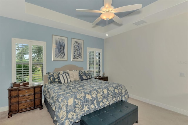 bedroom featuring ceiling fan, light colored carpet, and a tray ceiling