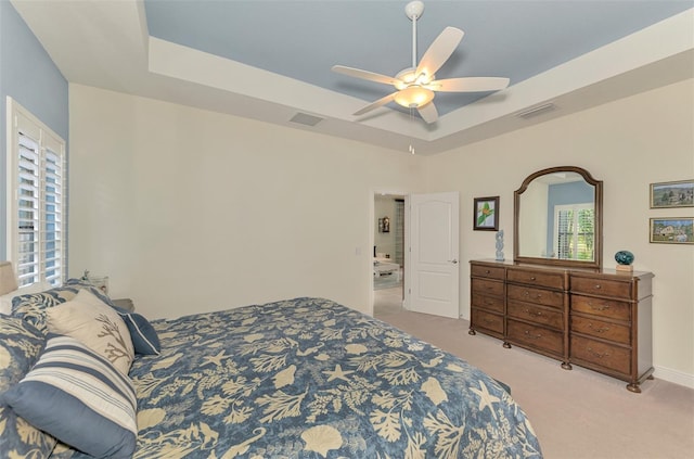 bedroom with light carpet, ceiling fan, and a tray ceiling