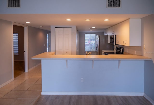 kitchen with white cabinetry, stainless steel appliances, kitchen peninsula, and a kitchen bar