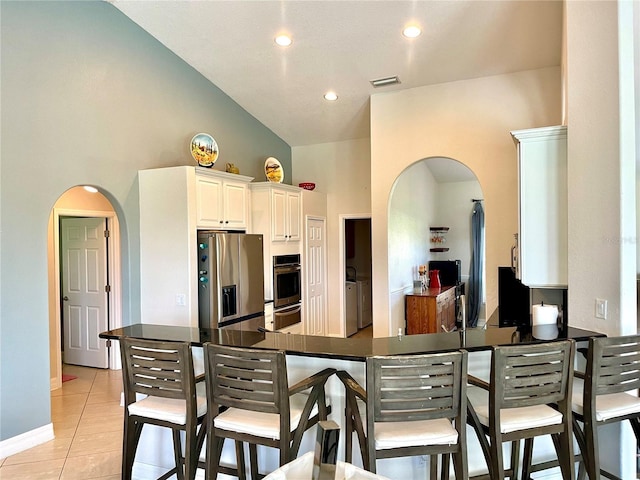 kitchen featuring light tile patterned floors, white cabinetry, high vaulted ceiling, stainless steel appliances, and kitchen peninsula