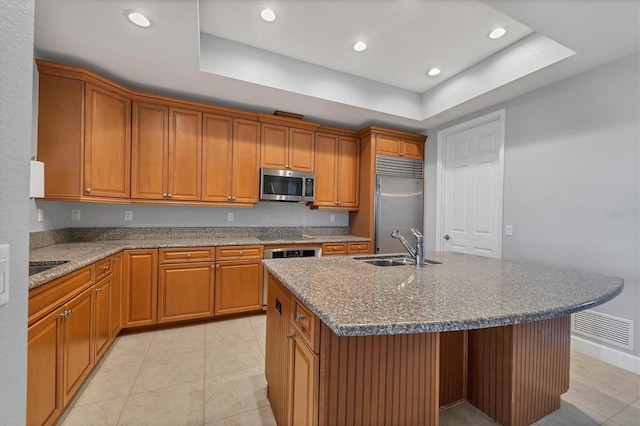 kitchen with sink, an island with sink, a raised ceiling, and appliances with stainless steel finishes