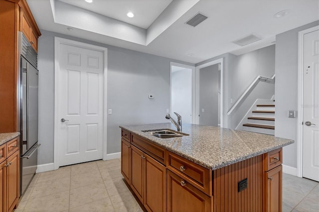 kitchen with light stone counters, high quality fridge, sink, and a kitchen island with sink