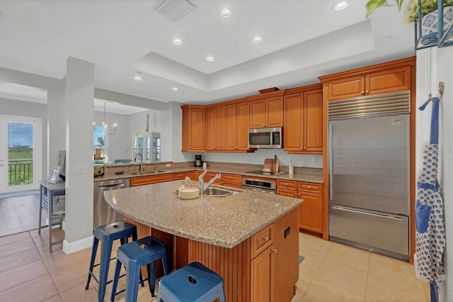 10360 Longshore Rd Unit 66, Placida, FL 33946 - kitchen featuring appliances with stainless steel finishes, a raised ceiling, a center island with sink, light tile patterned floors, and a breakfast bar area