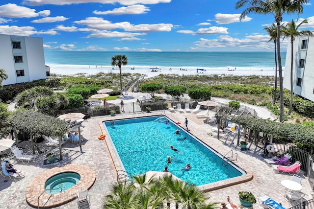 view of pool with a beach view, a water view, a hot tub, and a patio