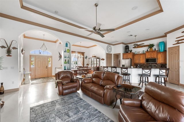 tiled living room with ceiling fan, a high ceiling, ornamental molding, and a tray ceiling