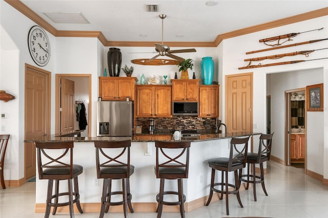 kitchen featuring a kitchen breakfast bar, stainless steel refrigerator with ice dispenser, tasteful backsplash, dark stone counters, and a kitchen island