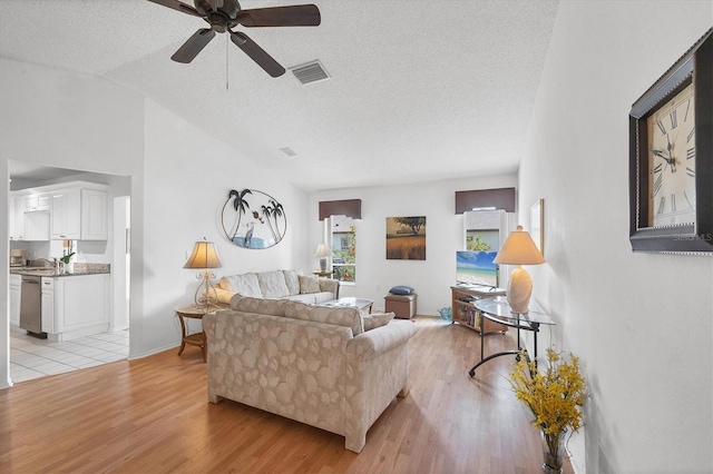 living room featuring ceiling fan, vaulted ceiling, a textured ceiling, and light wood-type flooring