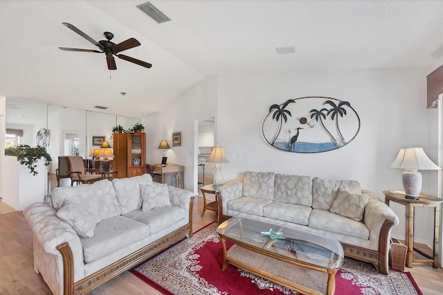 living room featuring ceiling fan, lofted ceiling, a textured ceiling, and light wood-type flooring