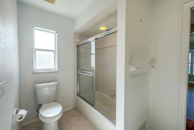 bathroom featuring bath / shower combo with glass door, tile patterned floors, and toilet