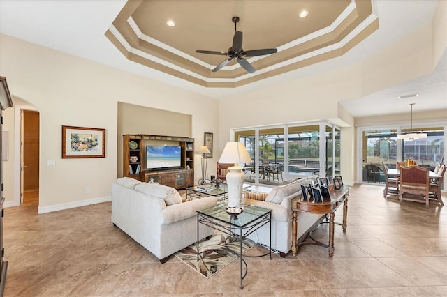 living room featuring crown molding, ceiling fan with notable chandelier, a high ceiling, and a raised ceiling