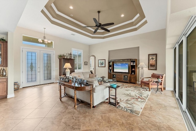 living room featuring ceiling fan with notable chandelier, french doors, crown molding, and a tray ceiling