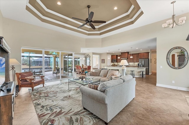 living room with ceiling fan with notable chandelier, a towering ceiling, a tray ceiling, and ornamental molding