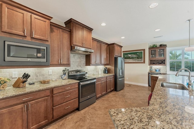 kitchen featuring appliances with stainless steel finishes, decorative light fixtures, decorative backsplash, sink, and light stone counters