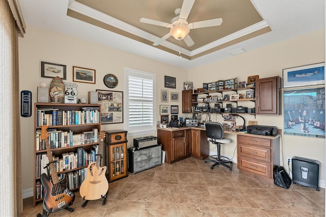 home office featuring ceiling fan, built in desk, ornamental molding, and a tray ceiling