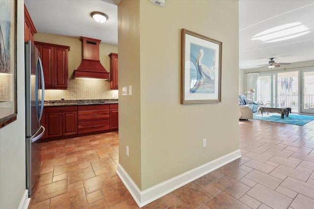 kitchen featuring premium range hood, stainless steel refrigerator, ceiling fan, dark stone counters, and decorative backsplash