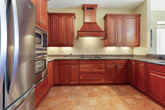 kitchen with sink, appliances with stainless steel finishes, dark stone countertops, decorative backsplash, and custom exhaust hood