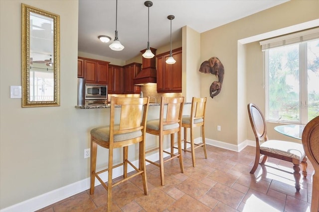 kitchen with light stone counters, hanging light fixtures, a kitchen breakfast bar, kitchen peninsula, and stainless steel appliances