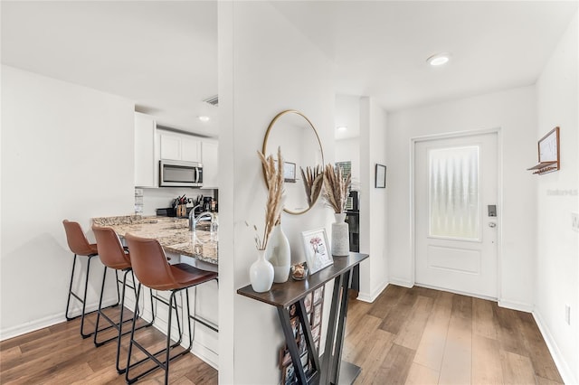 interior space featuring a kitchen bar, kitchen peninsula, hardwood / wood-style floors, white cabinets, and light stone counters