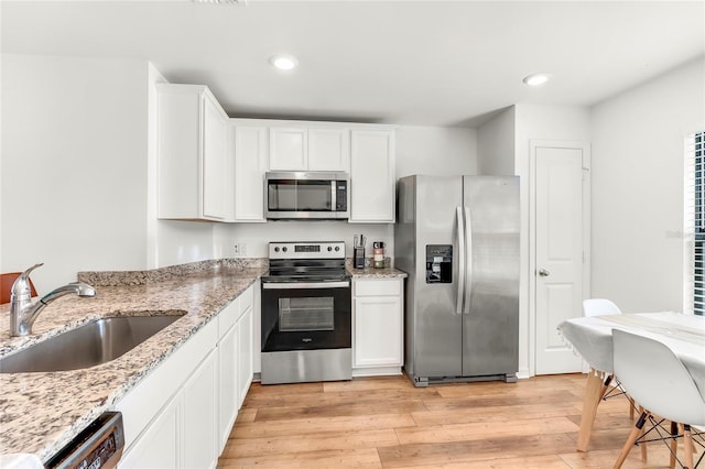 kitchen with light stone countertops, appliances with stainless steel finishes, white cabinetry, light hardwood / wood-style floors, and sink