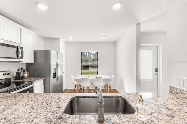 kitchen with hardwood / wood-style floors, white cabinetry, stainless steel appliances, sink, and light stone counters