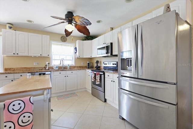 kitchen featuring sink, light tile patterned floors, ceiling fan, stainless steel appliances, and white cabinets