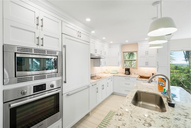 kitchen with built in appliances, sink, decorative light fixtures, and white cabinets