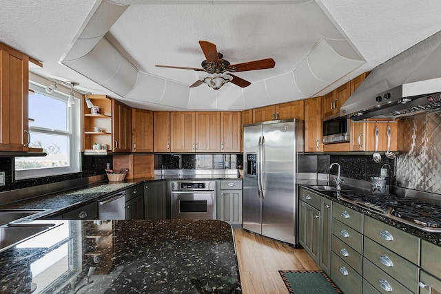 kitchen with sink, appliances with stainless steel finishes, dark stone countertops, a raised ceiling, and exhaust hood