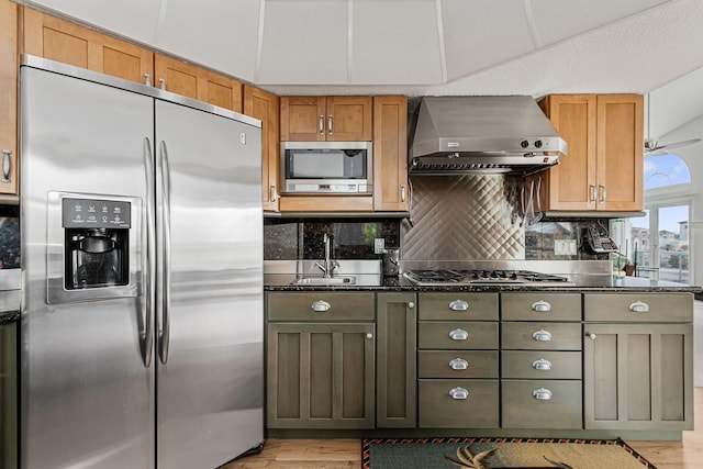 kitchen featuring appliances with stainless steel finishes, tasteful backsplash, sink, dark stone counters, and wall chimney range hood