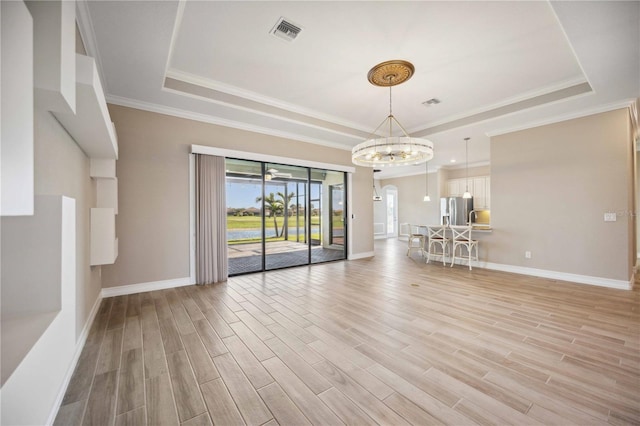 unfurnished living room with crown molding, a notable chandelier, a raised ceiling, and light wood-type flooring