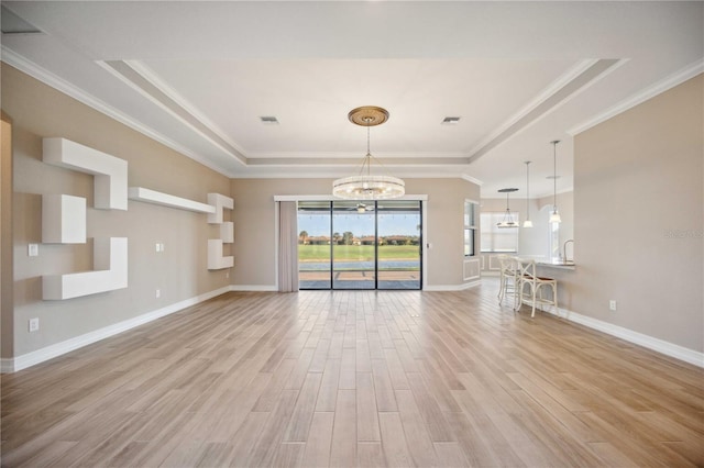 unfurnished living room with a notable chandelier, crown molding, light hardwood / wood-style floors, and a raised ceiling