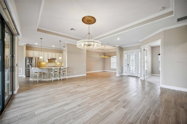 unfurnished living room featuring an inviting chandelier, a tray ceiling, light hardwood / wood-style flooring, and crown molding