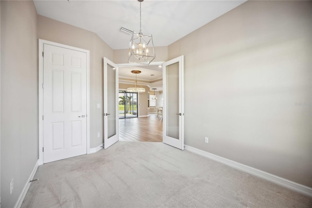 carpeted empty room with french doors, ornamental molding, and a chandelier