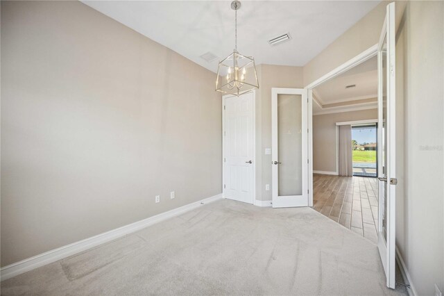 spare room with an inviting chandelier, ornamental molding, light carpet, and french doors