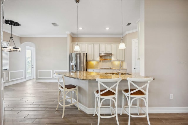 kitchen with a breakfast bar area, stainless steel fridge with ice dispenser, hanging light fixtures, light stone countertops, and backsplash