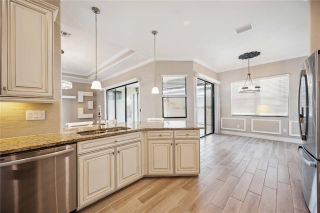 kitchen featuring pendant lighting, sink, stainless steel appliances, light stone countertops, and cream cabinetry