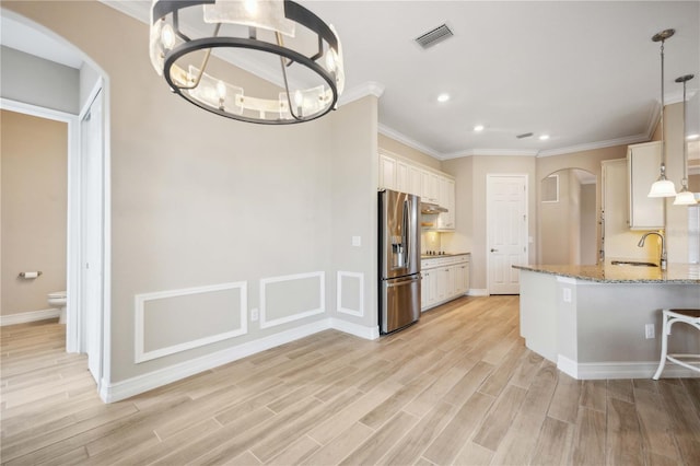 kitchen with decorative light fixtures, sink, stainless steel refrigerator with ice dispenser, light stone countertops, and light hardwood / wood-style flooring