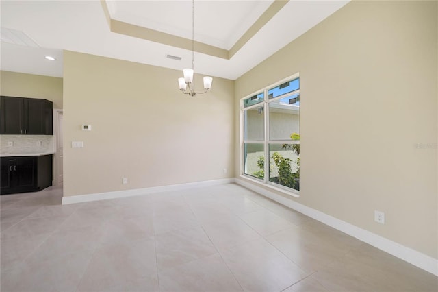 empty room featuring an inviting chandelier, a tray ceiling, and light tile patterned flooring