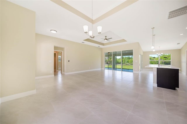 unfurnished living room with a tray ceiling, ceiling fan with notable chandelier, and light tile patterned floors