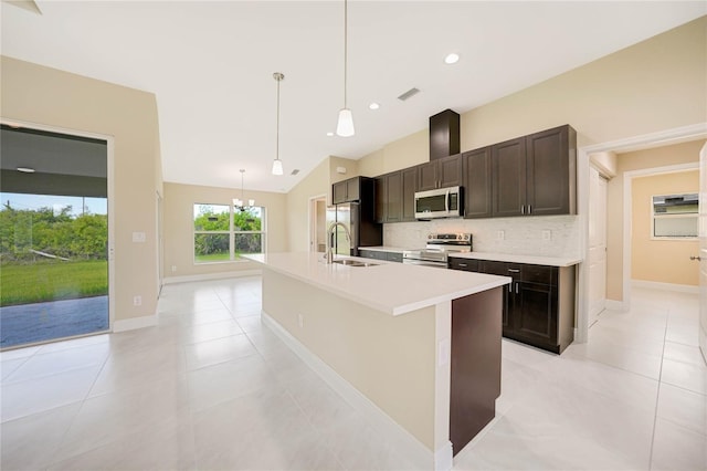 kitchen featuring appliances with stainless steel finishes, a kitchen island with sink, dark brown cabinets, tasteful backsplash, and decorative light fixtures