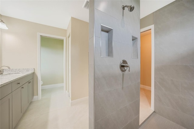 bathroom with tile patterned flooring, vanity, a tile shower, and toilet