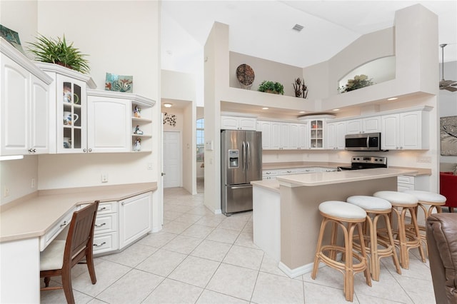 kitchen featuring light tile patterned floors, appliances with stainless steel finishes, white cabinetry, a kitchen island, and a kitchen bar