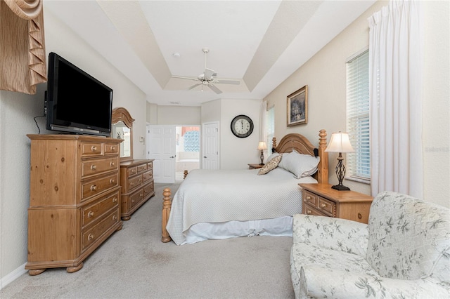 carpeted bedroom featuring ceiling fan, a tray ceiling, and ensuite bath