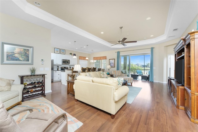 living room with ceiling fan, a tray ceiling, and hardwood / wood-style floors