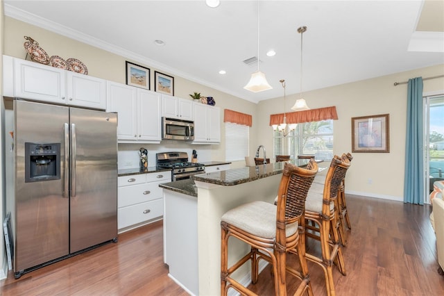 kitchen with hardwood / wood-style flooring, appliances with stainless steel finishes, white cabinetry, hanging light fixtures, and dark stone counters