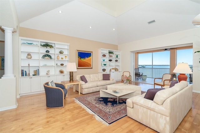 living room with built in shelves, ornate columns, a water view, vaulted ceiling, and light wood-type flooring