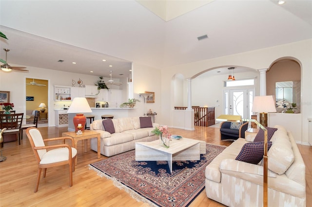 living room with a high ceiling, decorative columns, ceiling fan, and light wood-type flooring